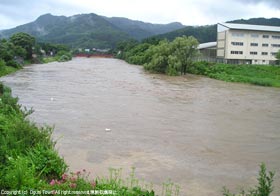 増水した横川横川右岸から小国小学校、小国大橋を望む写真